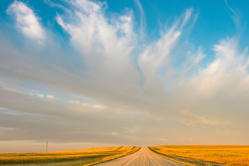 A vast prairie landscape in Saskatchewan with a rural road and dramatic clouds at sunset.