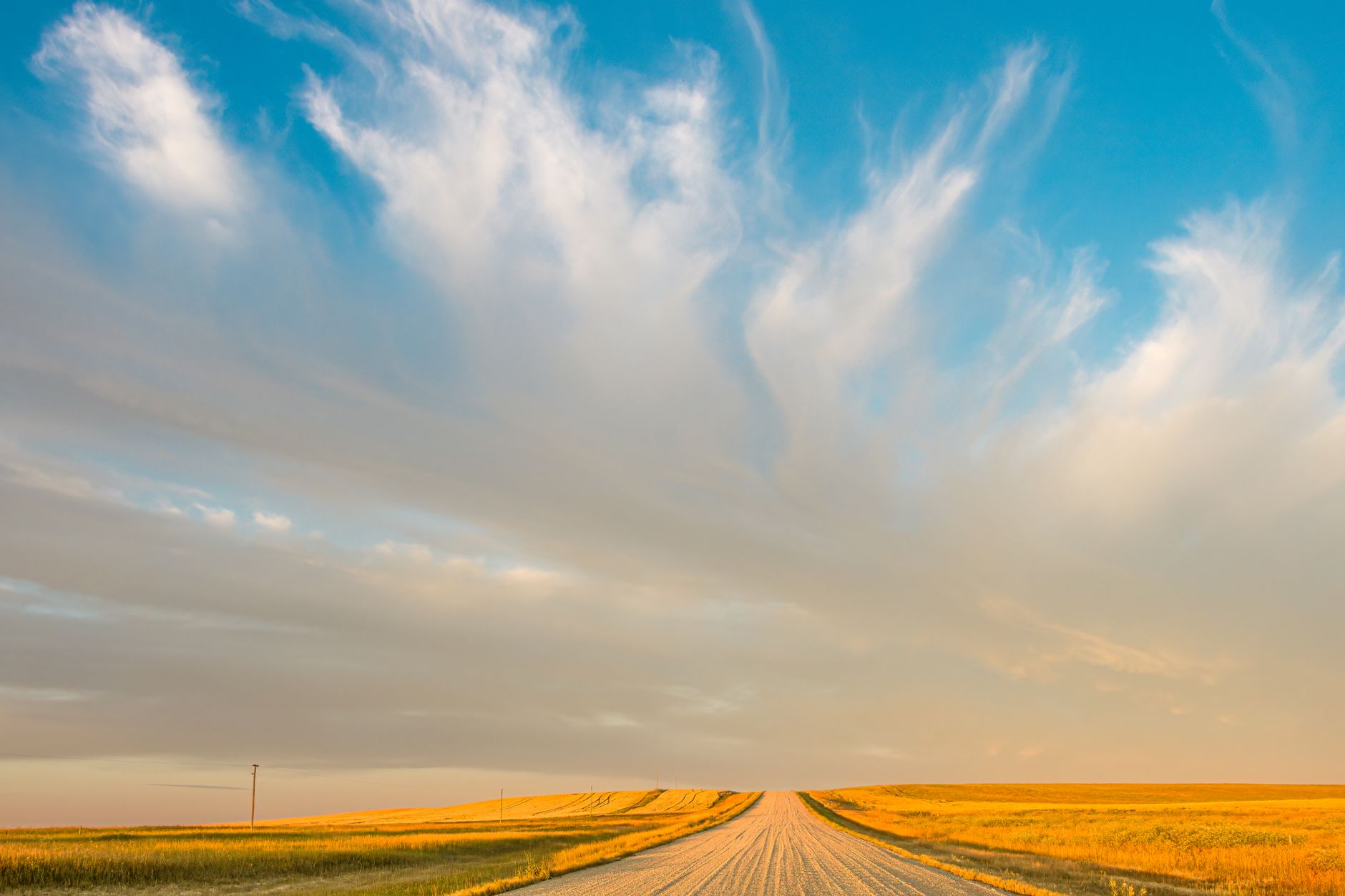 A vast prairie landscape in Saskatchewan with a rural road and dramatic clouds at sunset.