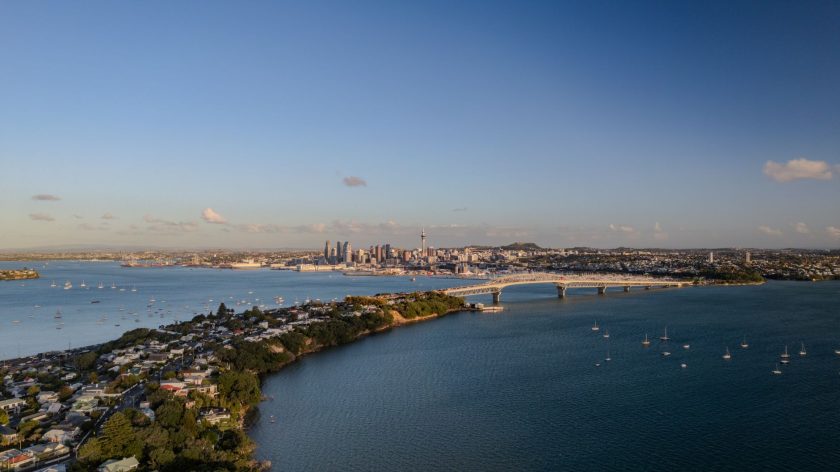 Aerial view of Auckland skyline, harbor, and bridge under clear sky.